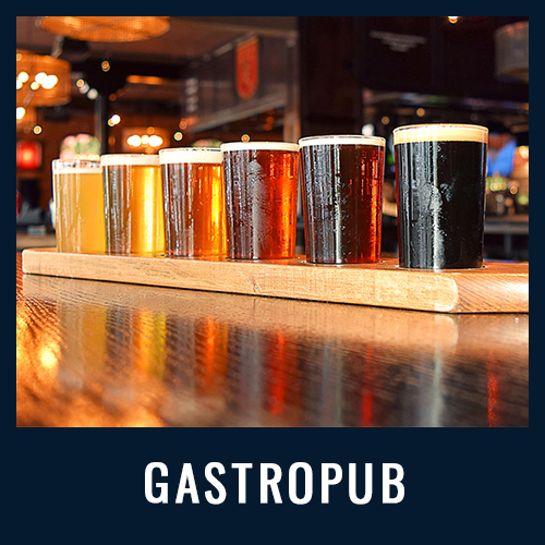 A wooden flight board with eight glasses of beer in various colors lined up on a glossy bar
