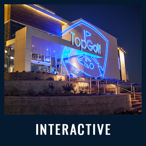 Exterior of a TopGolf venue at night, illuminated with bright blue neon lights