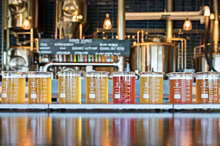 A colorful beer flight served in laboratory beakers, lined up on a bar