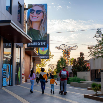 Families stroll through Grandscape outdoor shopping center at sunset.