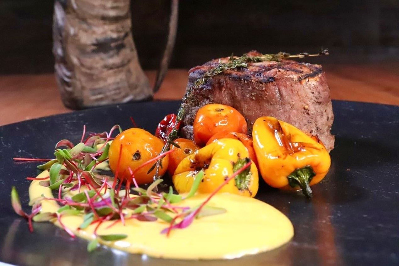 Grilled steak with baby peppers, microgreens and sauce served on a black plate.